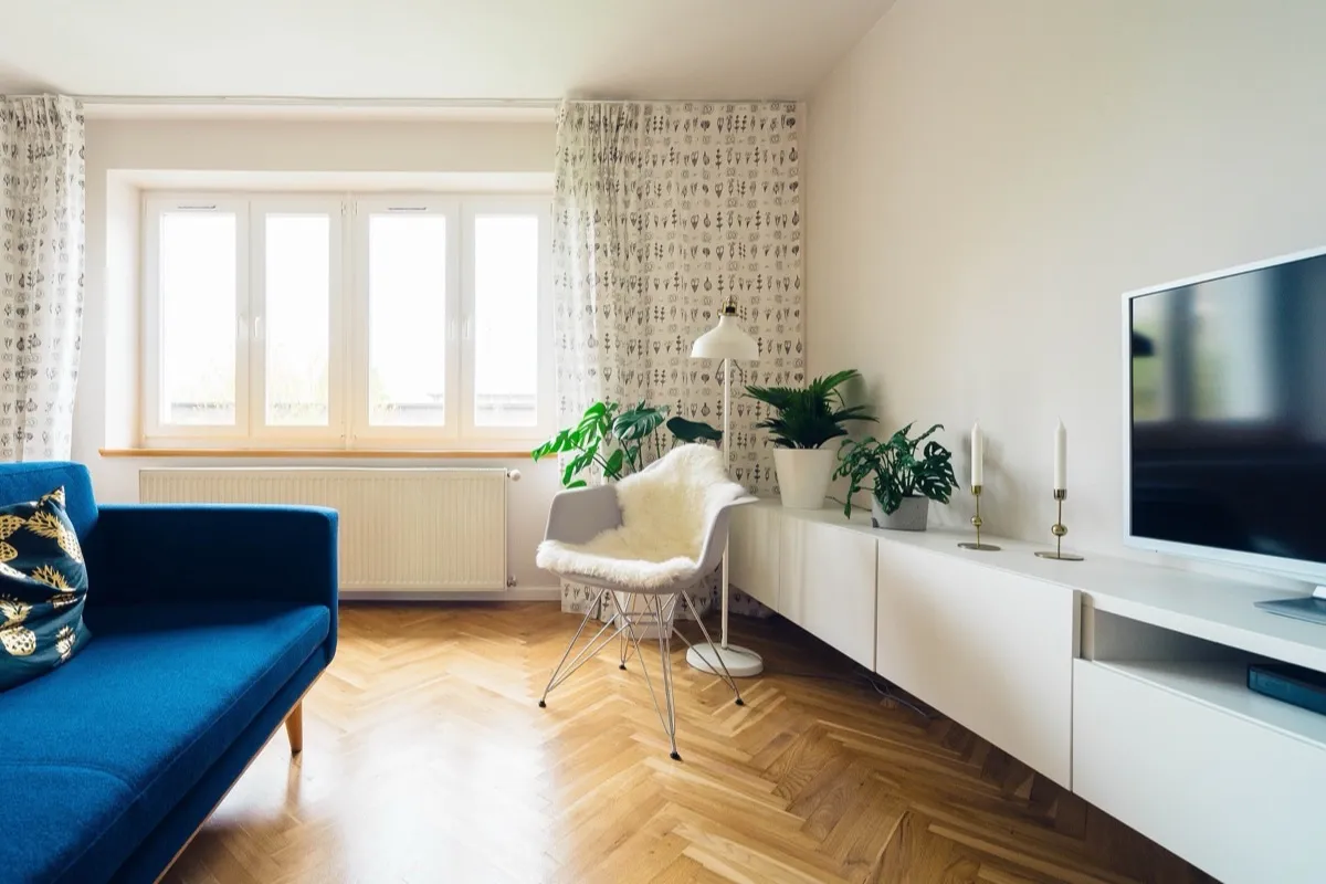 Sala con sofá azul, piso de madera y ventanal al jardín